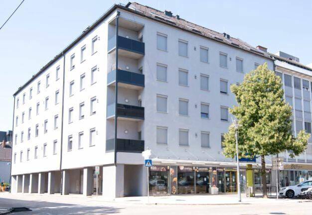 Mehrstöckiges Gebäude mit Ladenflächen im Erdgeschoss und Wohnungen darüber, inklusive Balkonen.