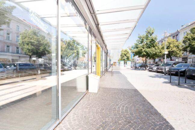 Blick entlang der Ladenfront eines Supermarktes mit großen Schaufenstern und einem gepflasterten Gehweg.