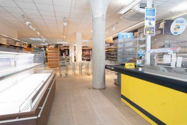 Kassenbereich eines Supermarktes mit gelber Kasse, leeren Regalen und Säulenstützen.