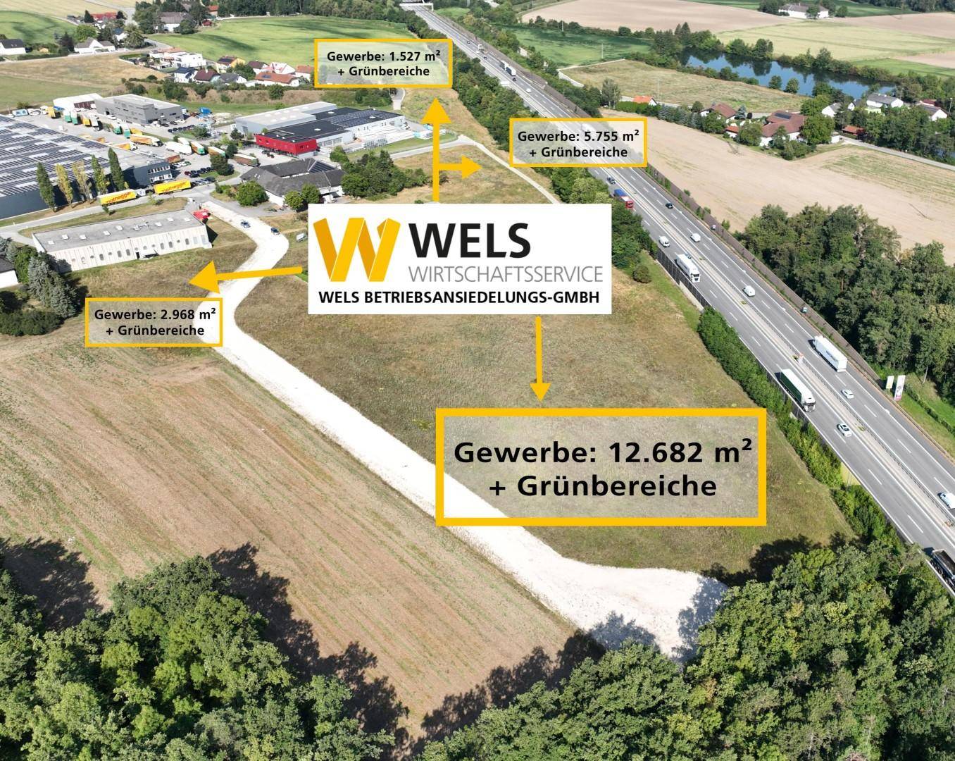 Luftaufnahme eines Gewerbegebiets neben einer Autobahn mit verschiedenen Parzellen und angrenzenden Grünflächen.