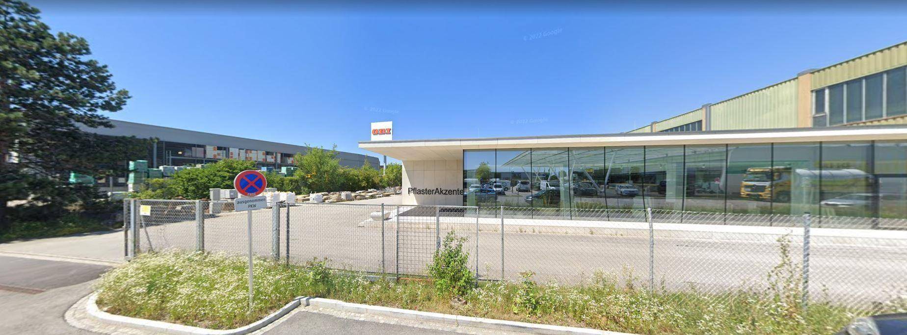 Modernes Geschäftsgebäude mit großer Glasfassade und einem Parkplatz im Vordergrund unter blauem Himmel.