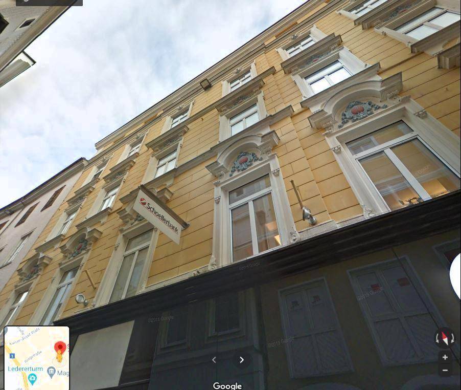 Historische gelbe Gebäudefassade mit einer Bankfiliale und verzierten Fenstern, aufgenommen aus der Straßenperspektive.