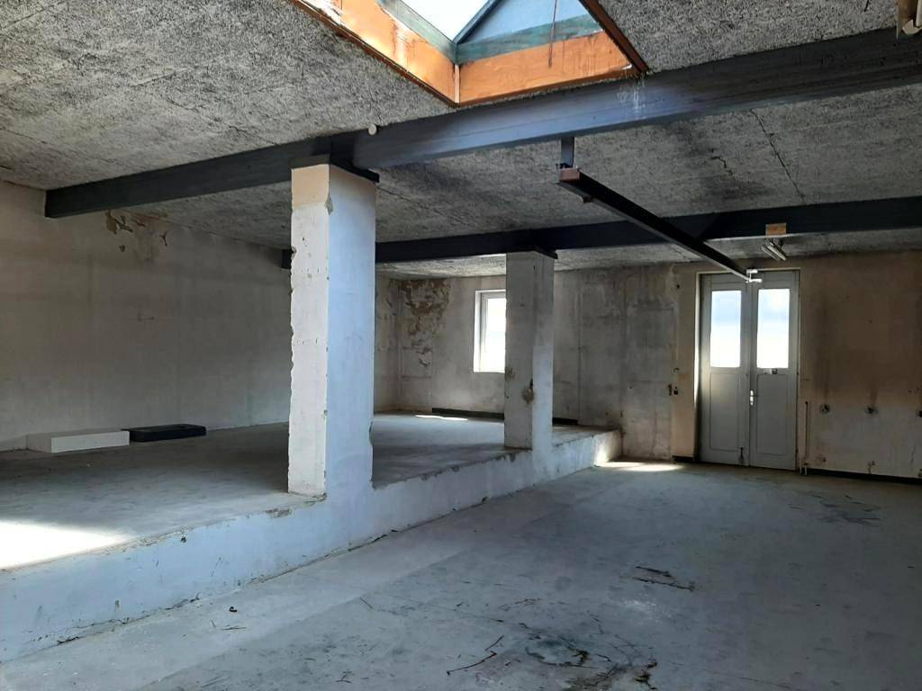 Weiterer Blick in den weitläufigen, unfertigen Raum mit Betonboden, Säulen und einem erhöhten Bereich.
