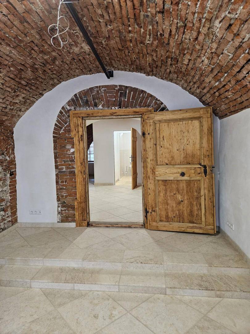 Historischer Raum mit beeindruckendem Ziegelgewölbe, hellen Fliesen und einer großen Holztür zu einem weiteren Bereich.