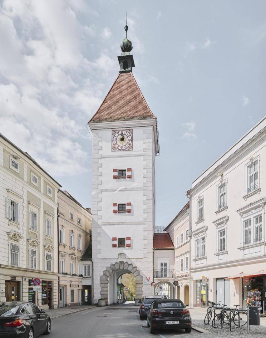 Historischer Uhrturm mit markantem Torbogen in einer malerischen Gasse, umgeben von traditionellen Gebäuden.