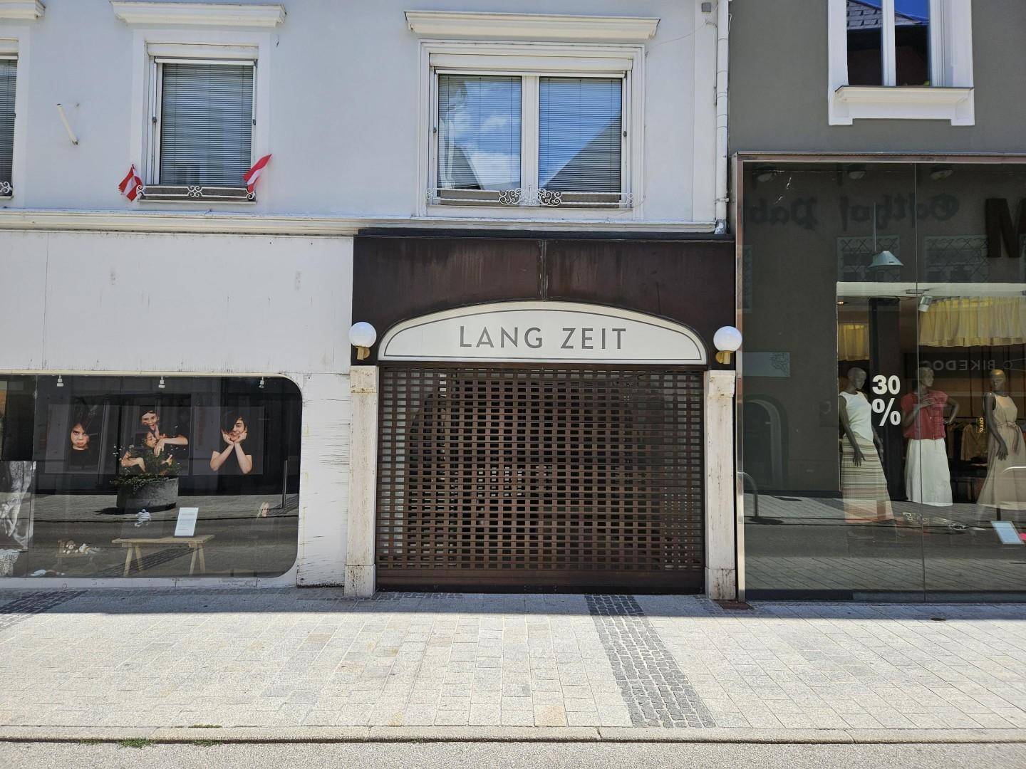 Ansicht der Ladenfassade mit einem geschlossenen Geschäft und Fenstern im ersten Stock, aufgenommen von der Straße.