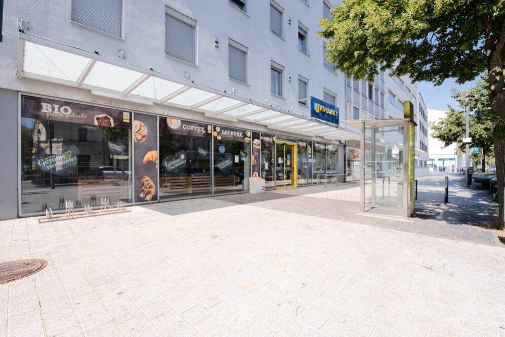 Geschäftsfront des Gebäudes mit großen Schaufenstern und einem überdachten Eingangsbereich an der Straße.