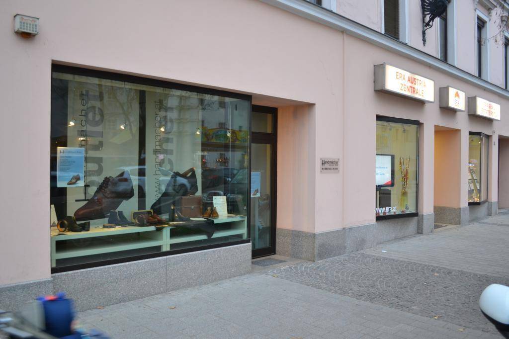 Geschäftsfassade mit Schaufenster und weiteren Ladenlokalen in einer belebten Einkaufsstraße.