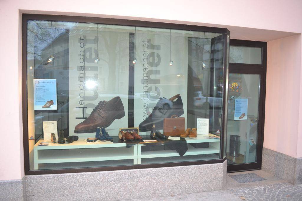 Schaufenster eines Ladens mit Herrenschuhen und Accessoires, gut beleuchtet.