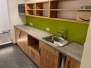 Kleine Küchenzeile mit Holzschränken, grüner Rückwand, Spüle und integriertem Ofen.