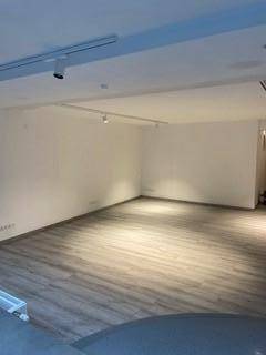 Leerer Gewerberaum mit hellem Holzoptikboden und moderner Schienenbeleuchtung an der Decke.