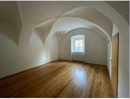 Langer Raum mit einem Fenster, das Tageslicht hereinlässt, einem schönen Holzdielenboden und einer markanten Gewölbedecke.