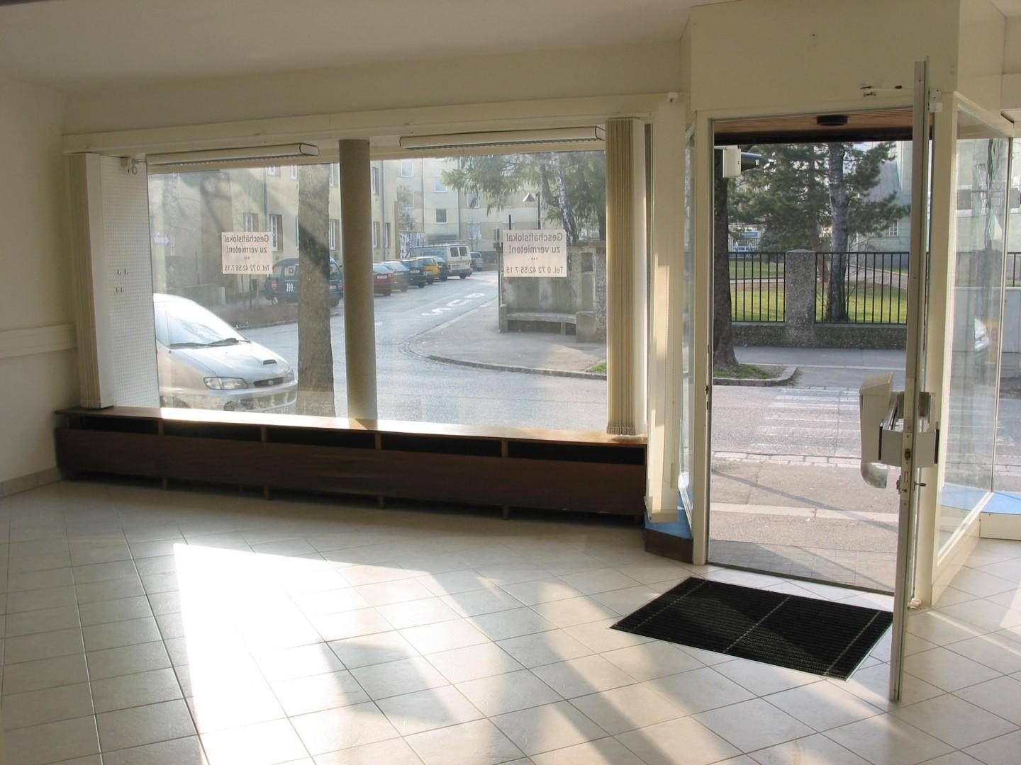 Heller, leerer Geschäftsraum mit großen Schaufenstern und Fliesenboden, Blick zur Straße.