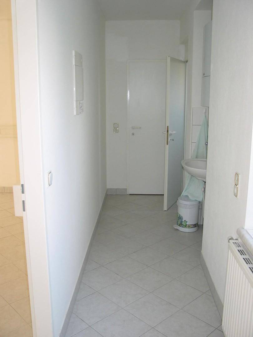 Heller Flur mit Fliesenboden, weißen Wänden und Zugang zu einem Badezimmer.