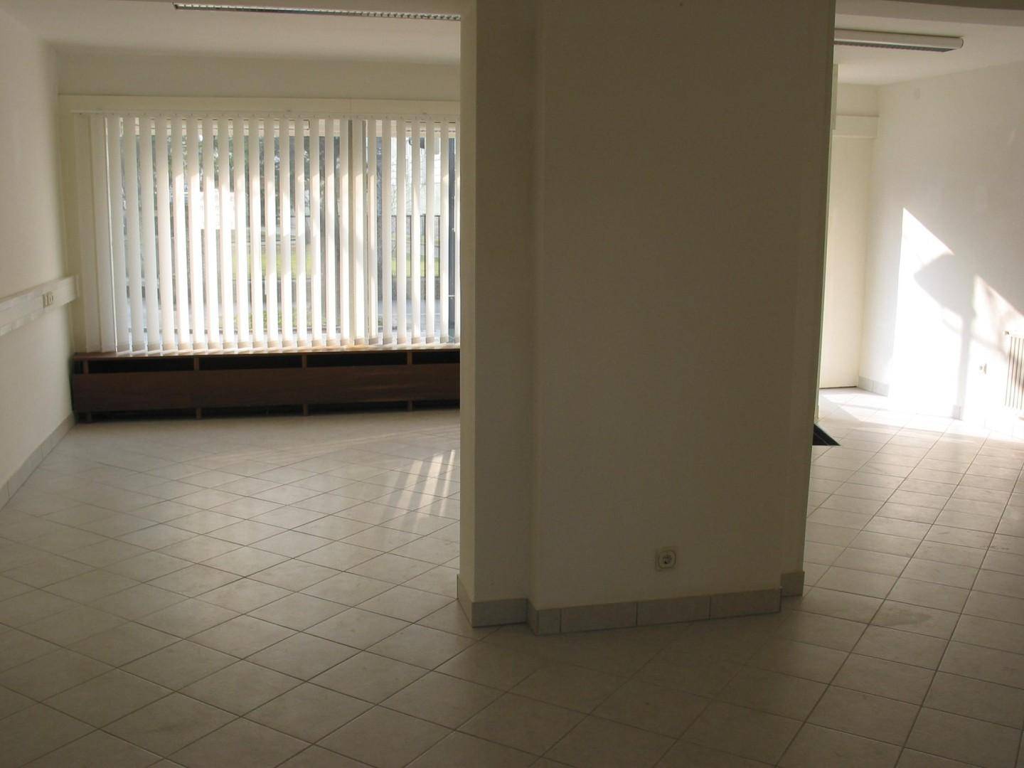Geräumiger, leerer Geschäftsraum mit Fliesenboden und vertikalen Jalousien an den Fenstern.