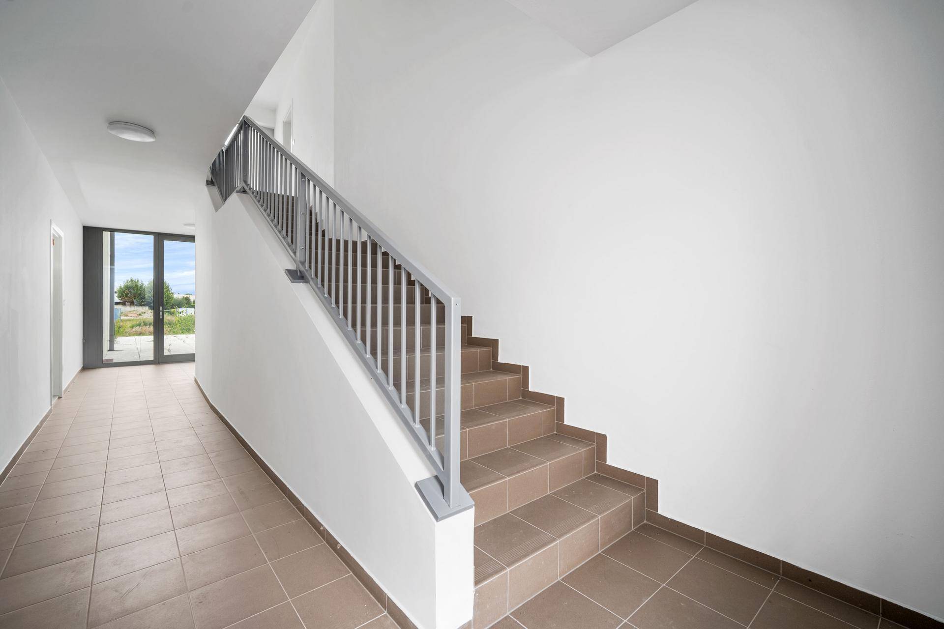 Heller Treppenaufgang mit Fliesenboden und modernem Geländer in einem Mehrfamilienhaus.