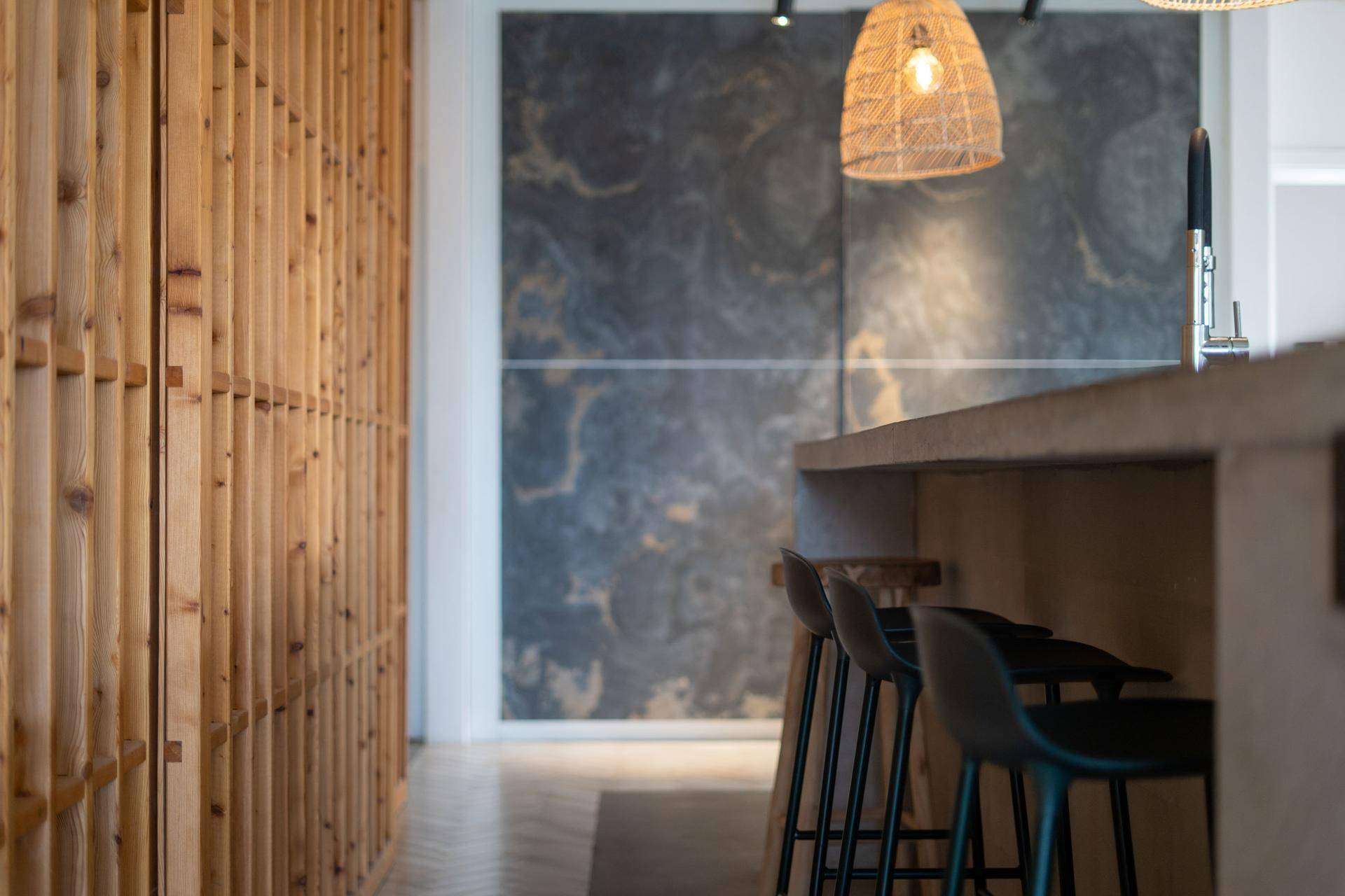 Detail der Kücheninsel mit Barhockern und der dekorativen Holzwandverkleidung.