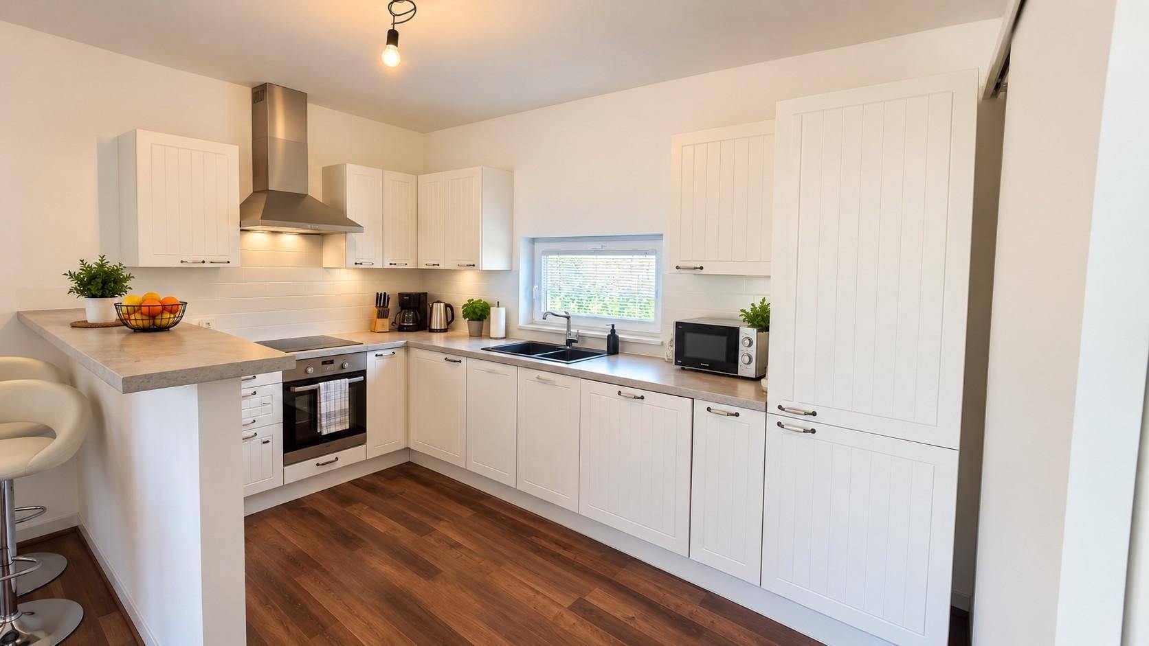 Moderne weiße Küche mit Holzboden, integrierten Geräten und Frühstücksbar.