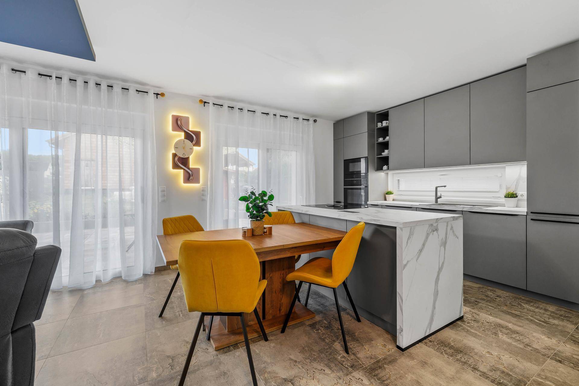 Offener Wohn-Essbereich mit moderner grauer Küche, Kücheninsel und gelben Akzenten.