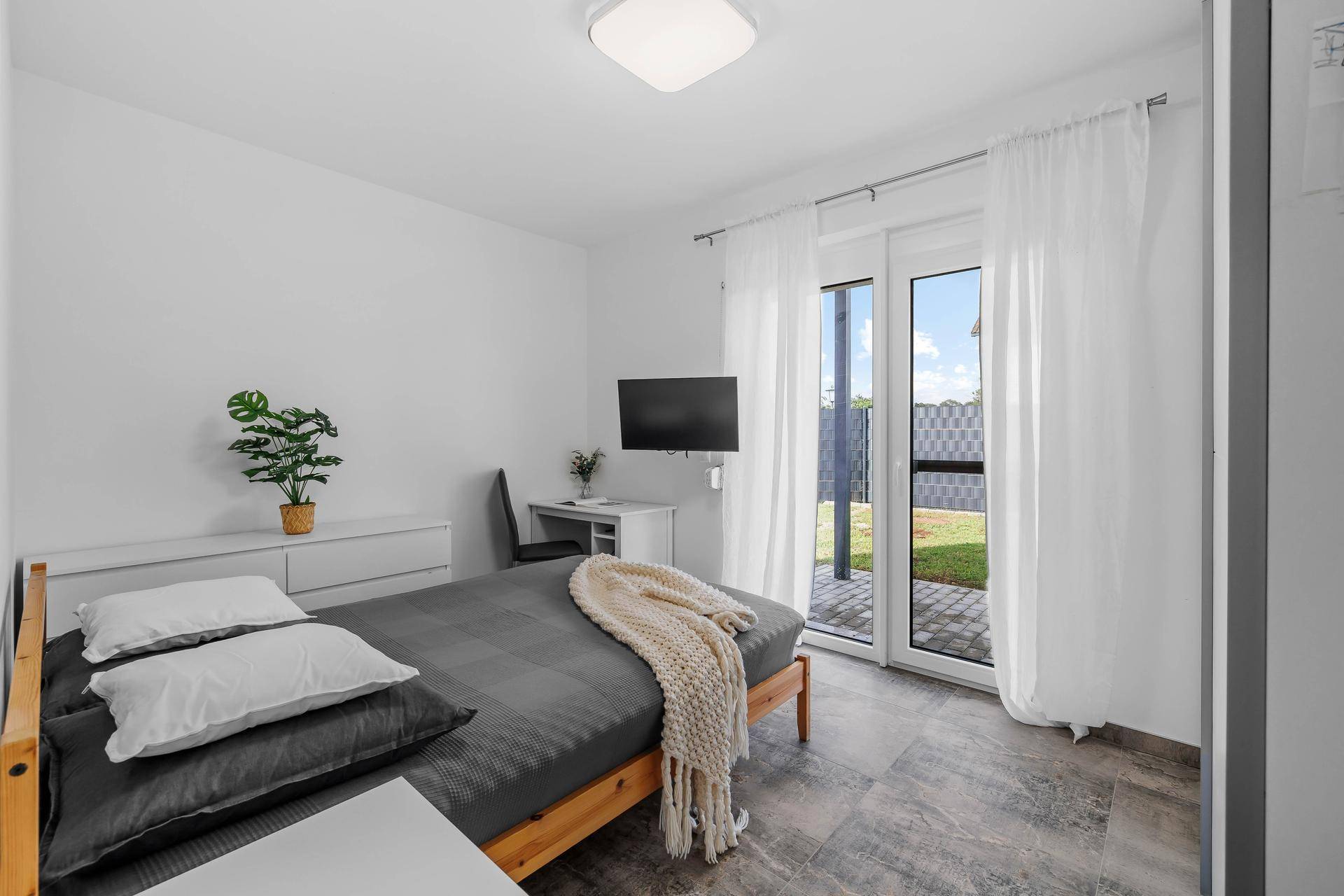 Helles Schlafzimmer mit direktem Zugang zum Garten, modernem Bett und Schreibtisch.