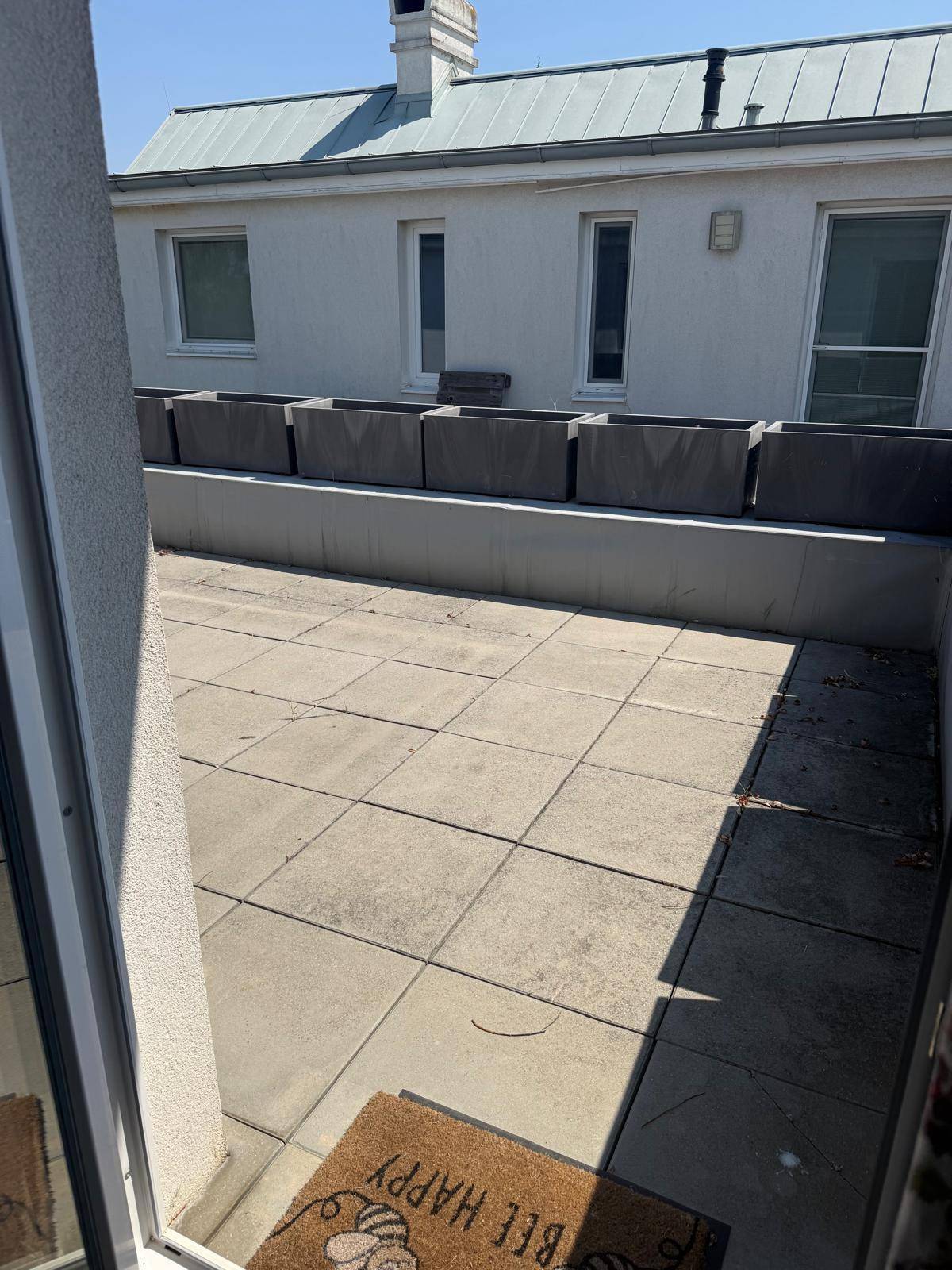 Geräumige Dachterrasse mit Fliesenboden und Blick auf das Gebäude.