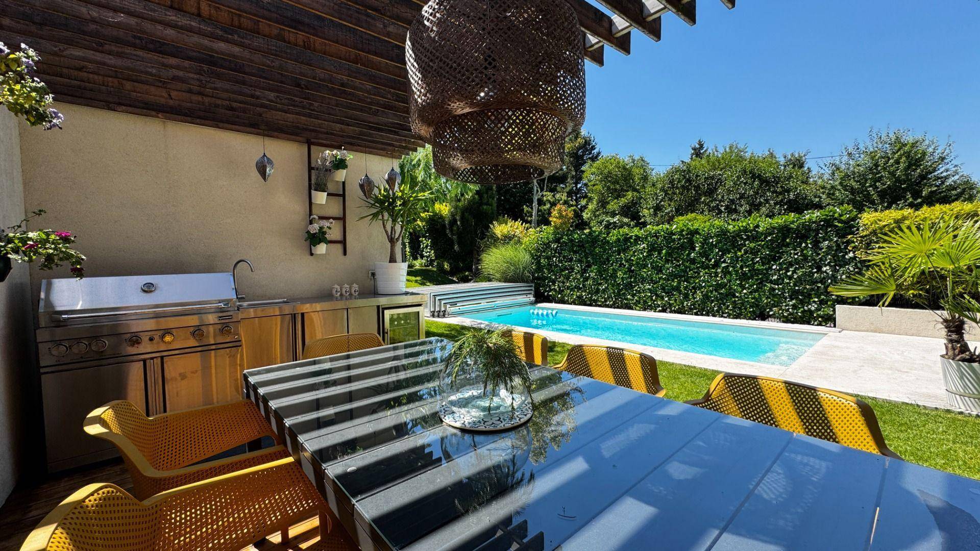 Sonniger Essbereich im Freien mit großem Tisch, Stühlen und einer voll ausgestatteten Außenküche neben dem Pool.