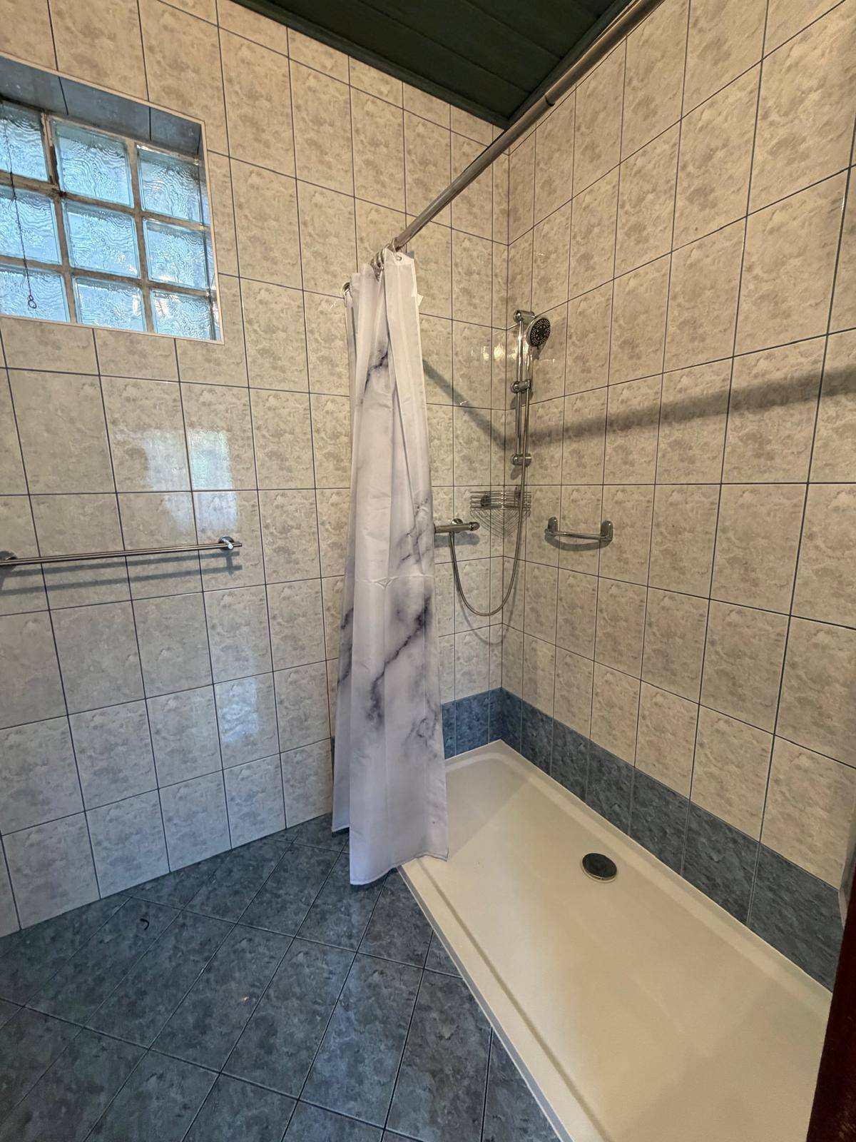 Duschbereich im Badezimmer mit Fliesen, Duschvorhang und Haltegriffen.