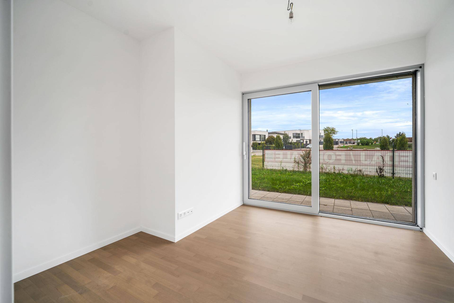 Leeres Schlafzimmer mit hellem Parkettboden und großem Fenster zum Garten.