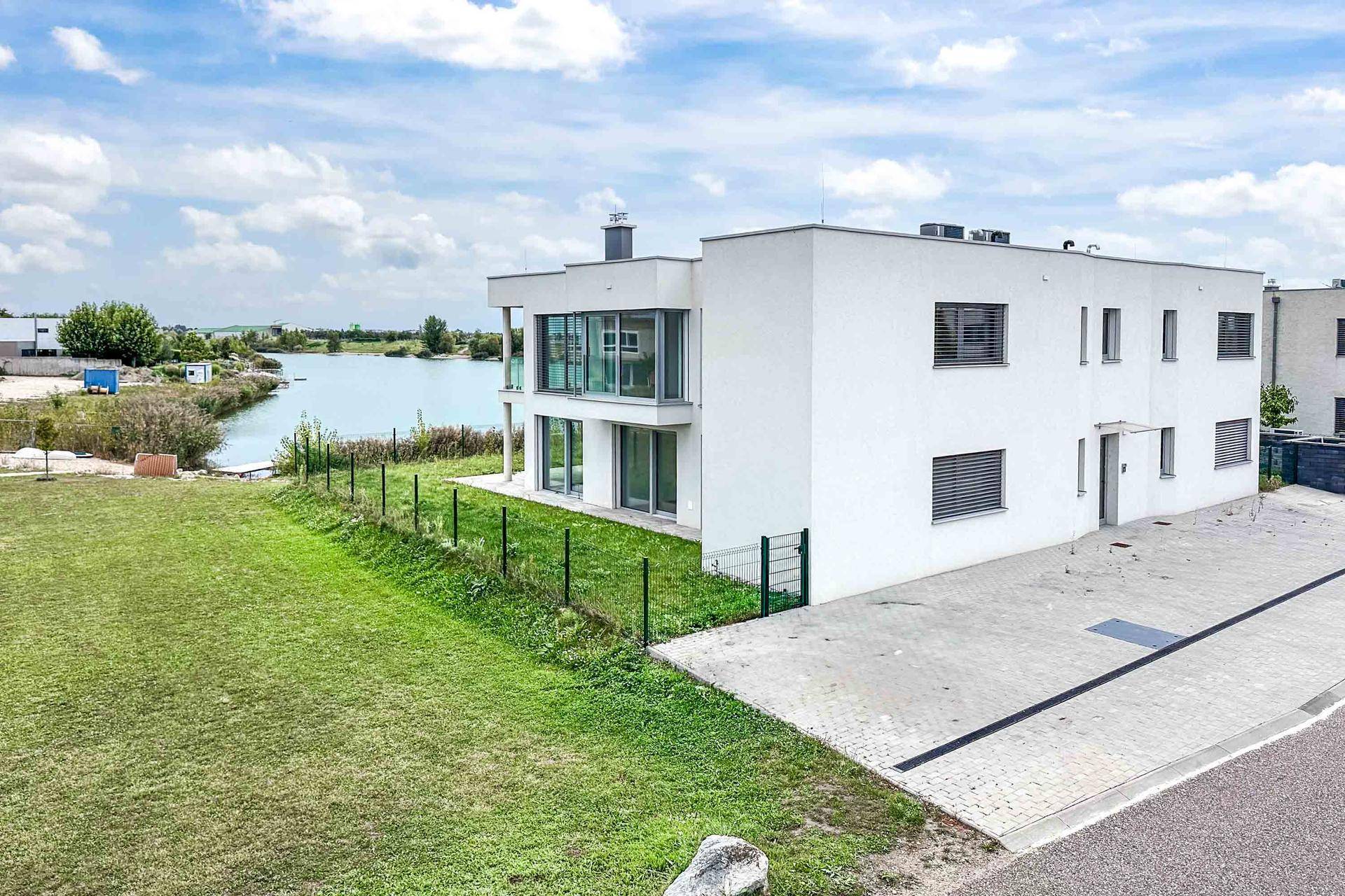 Zeitgenössisches weißes Gebäude mit Seeblick und gepflastertem Parkplatz vor dem Eingangsbereich.