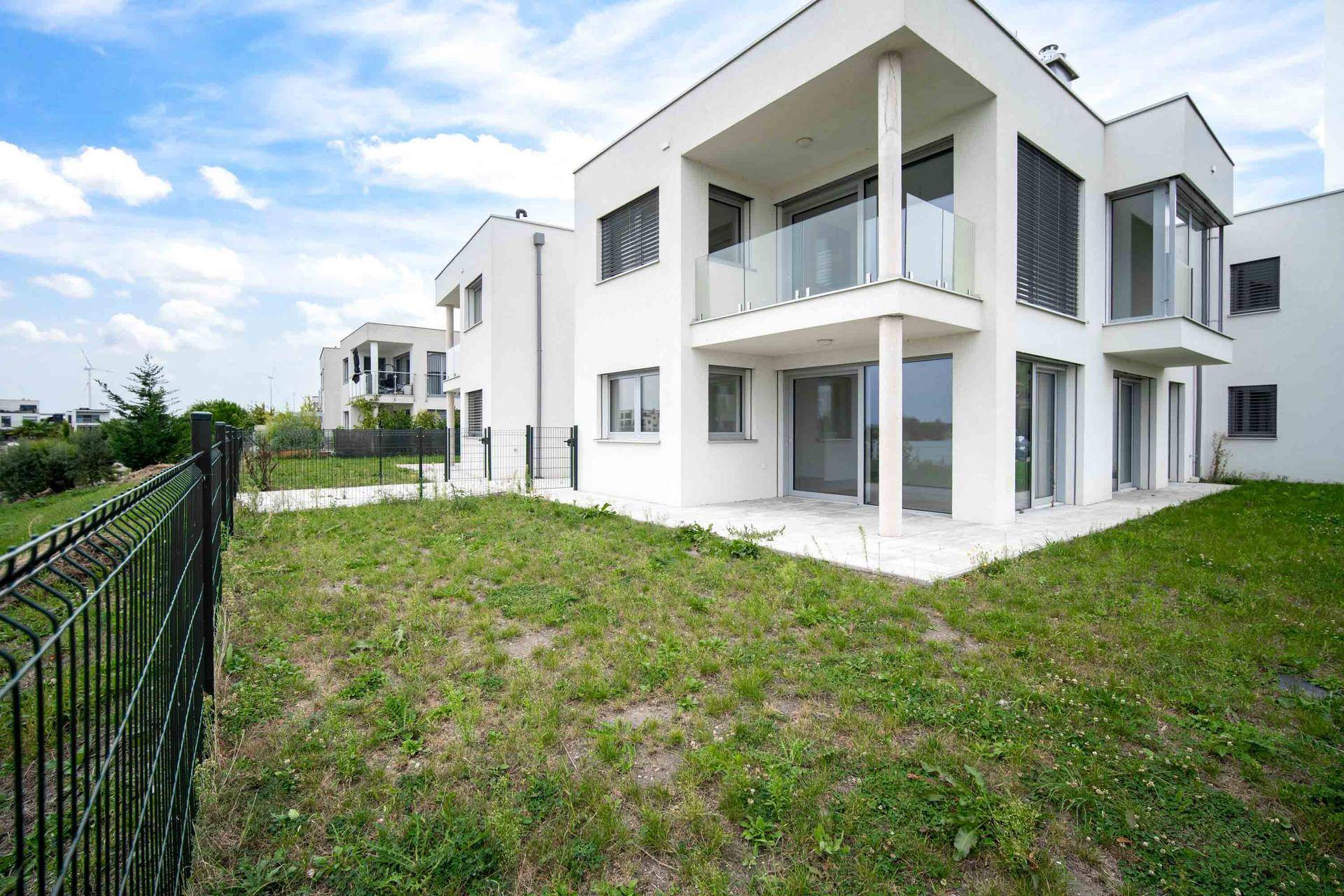 Seitenansicht des Gebäudes mit Garten, Terrasse und Balkon, umgeben von Grünflächen.