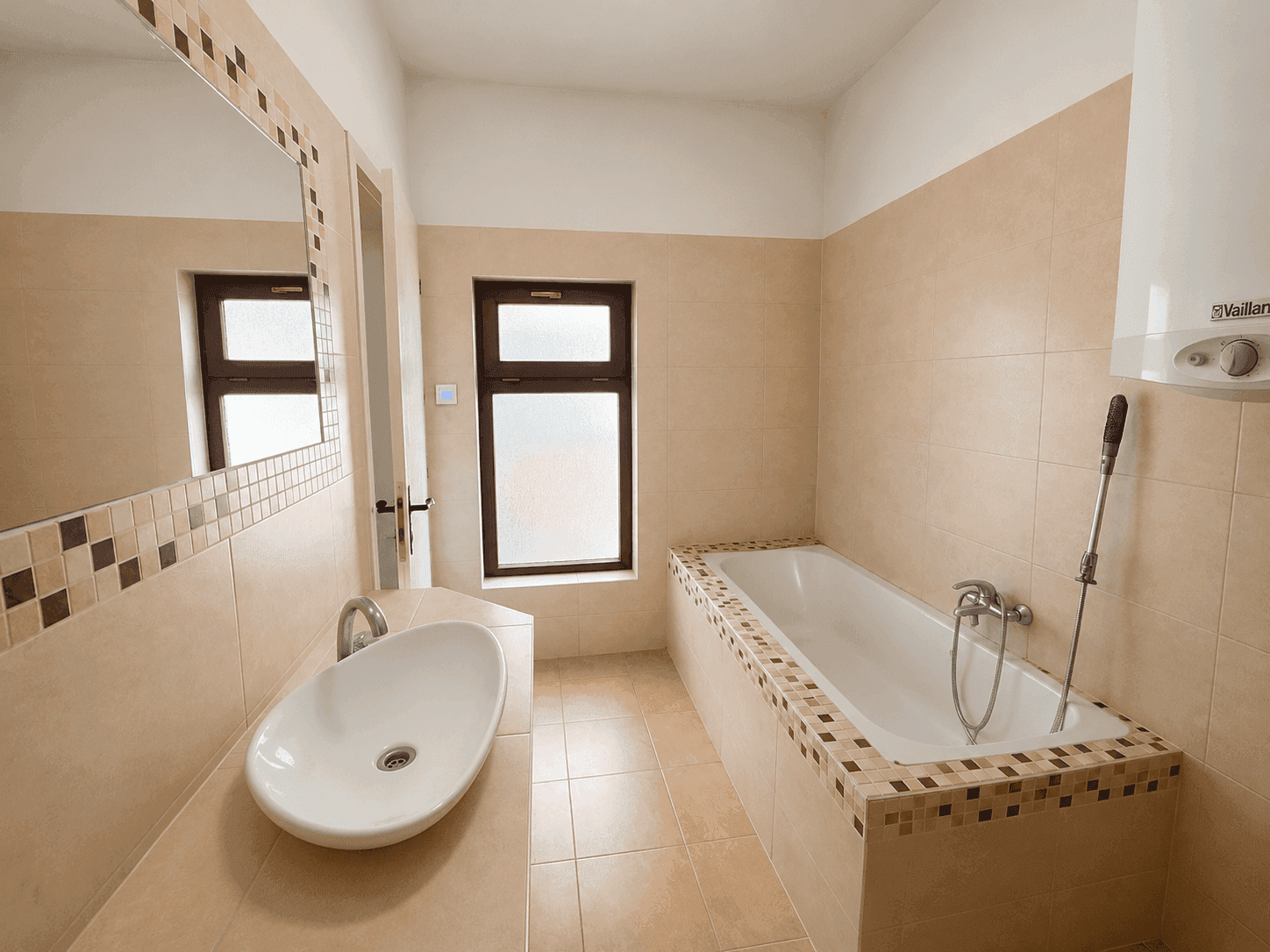 Badezimmer mit beigefarbenen Fliesen, Badewanne, Einzelwaschbecken und einem Fenster für Tageslicht.