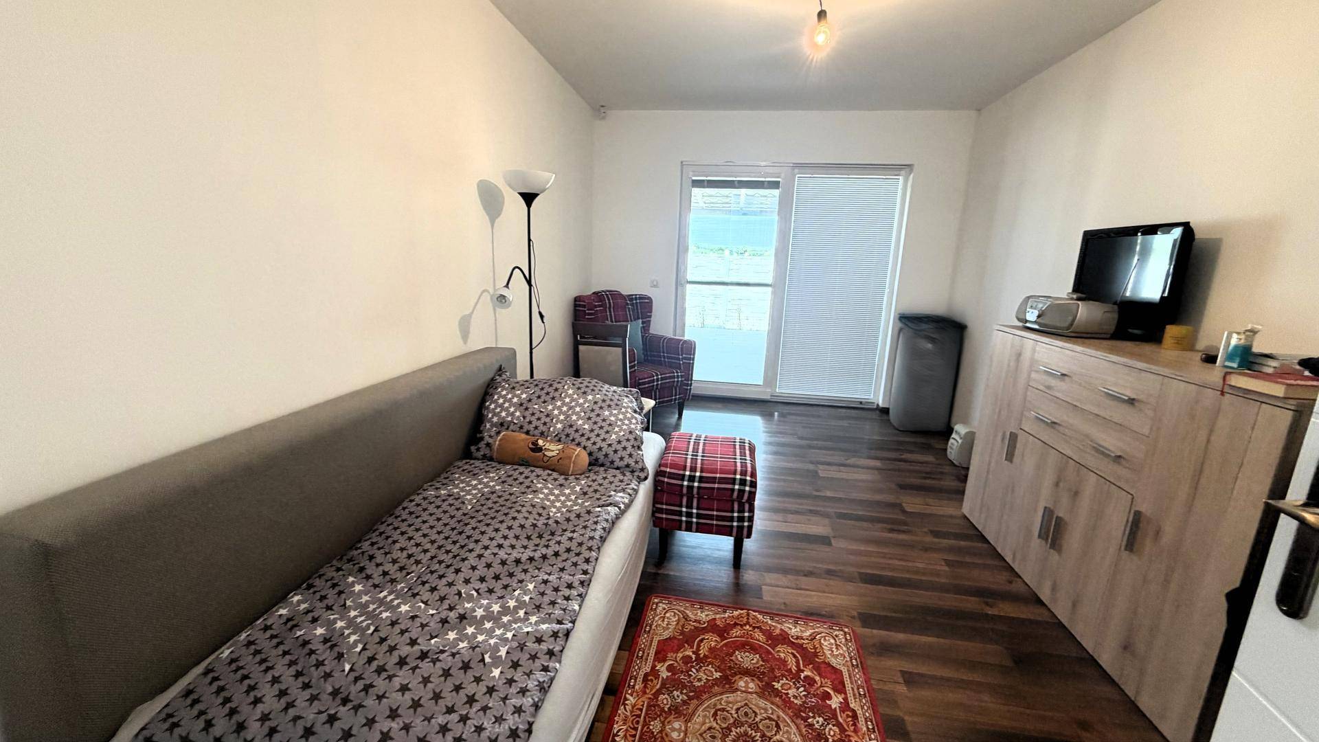 Einfaches Schlafzimmer mit Einzelbett, Schrank und Zugang zum Außenbereich.