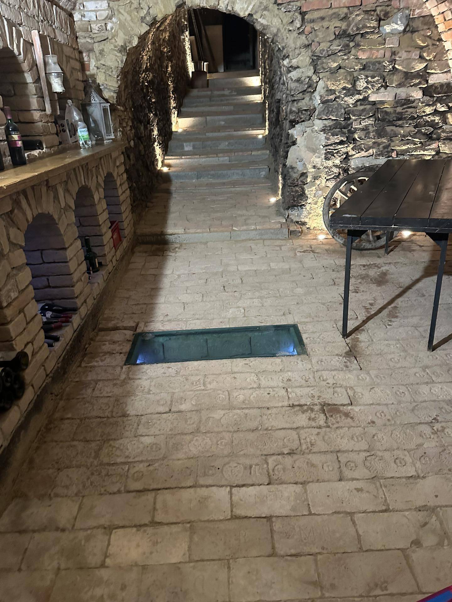 Blick in den Weinkeller mit Steintreppe, gemauerten Nischen und einem Tischbereich.