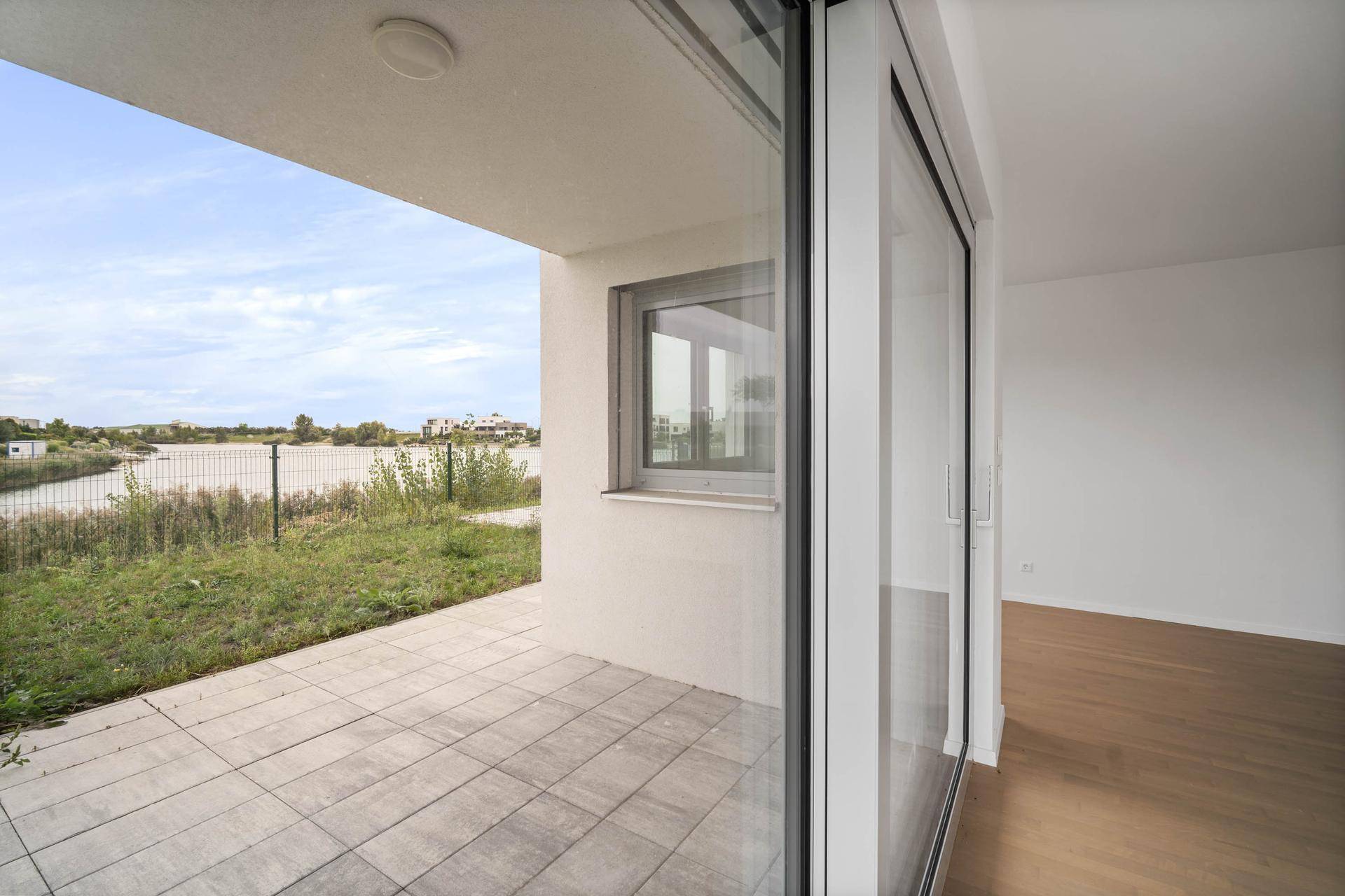 Terrasse mit Fliesenboden und Blick auf einen See, zugänglich durch große Fenster.