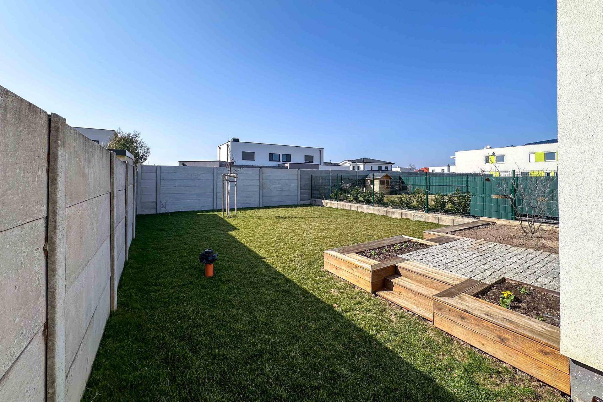 Hinterer Gartenbereich mit Rasenfläche, Betonzaun und erhöhten Pflanzbeeten.