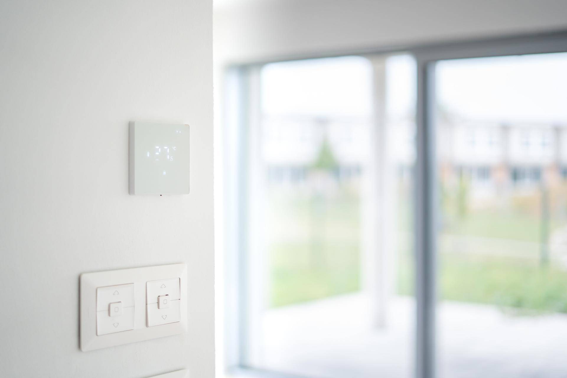 Nahaufnahme eines modernen Thermostats und Lichtschaltern an einer weißen Wand.