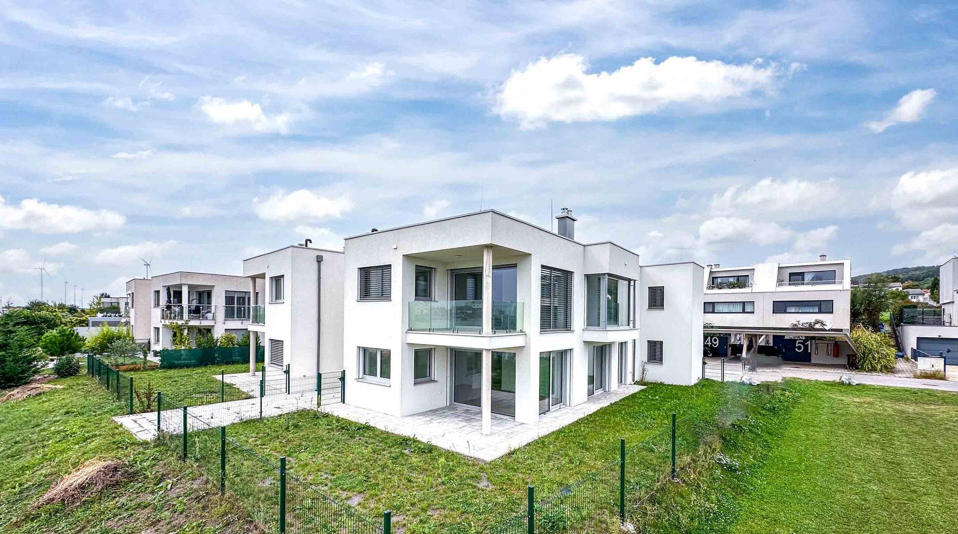 Moderne weiße Architektur mit großen Fenstern und Balkonen, umgeben von grünen Rasenflächen.