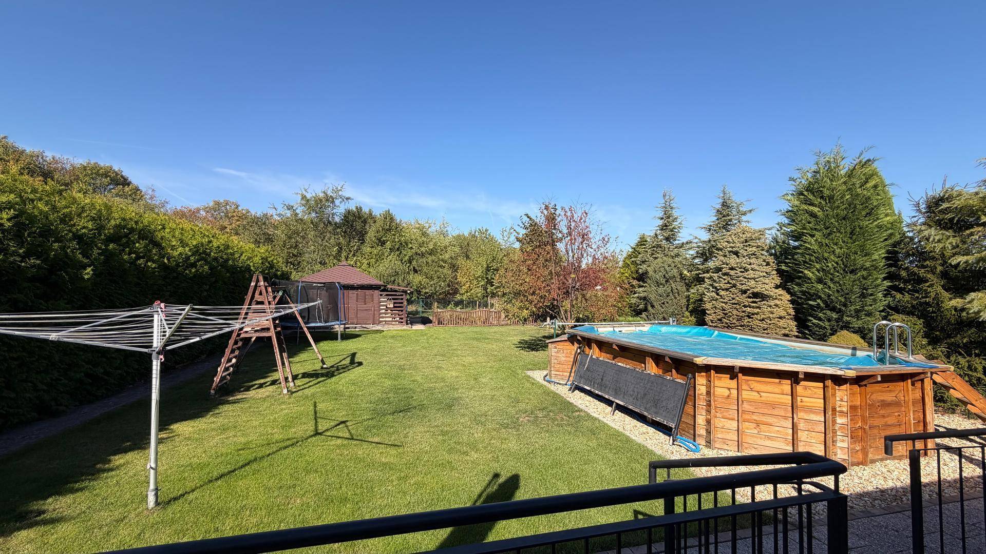 Weitläufiger Garten mit Rasenfläche, Pool und Kinderspielgeräten unter blauem Himmel.