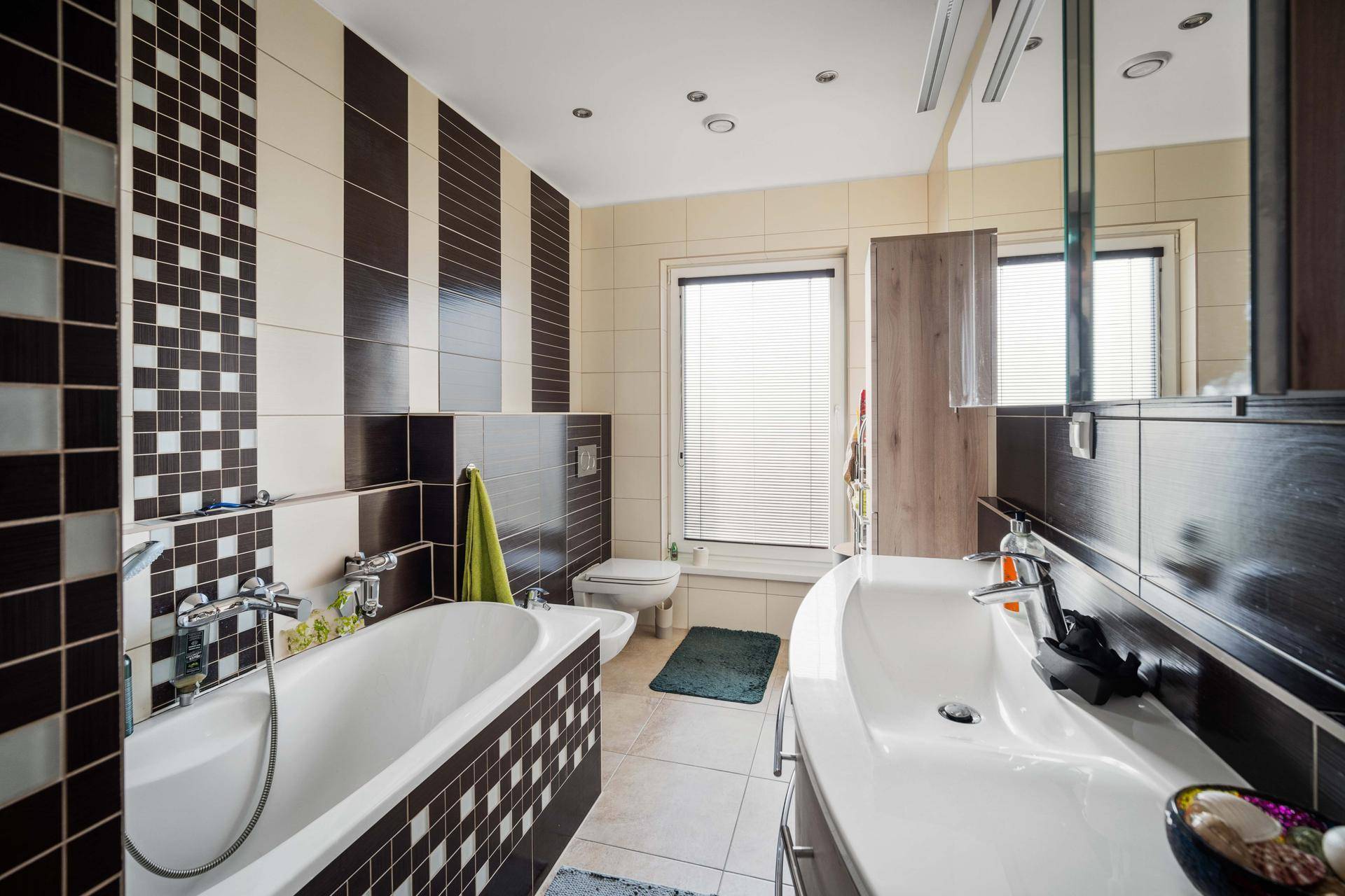 Badezimmer mit Badewanne, Doppelwaschbecken und dekorativen Fliesen in Braun-Beige.