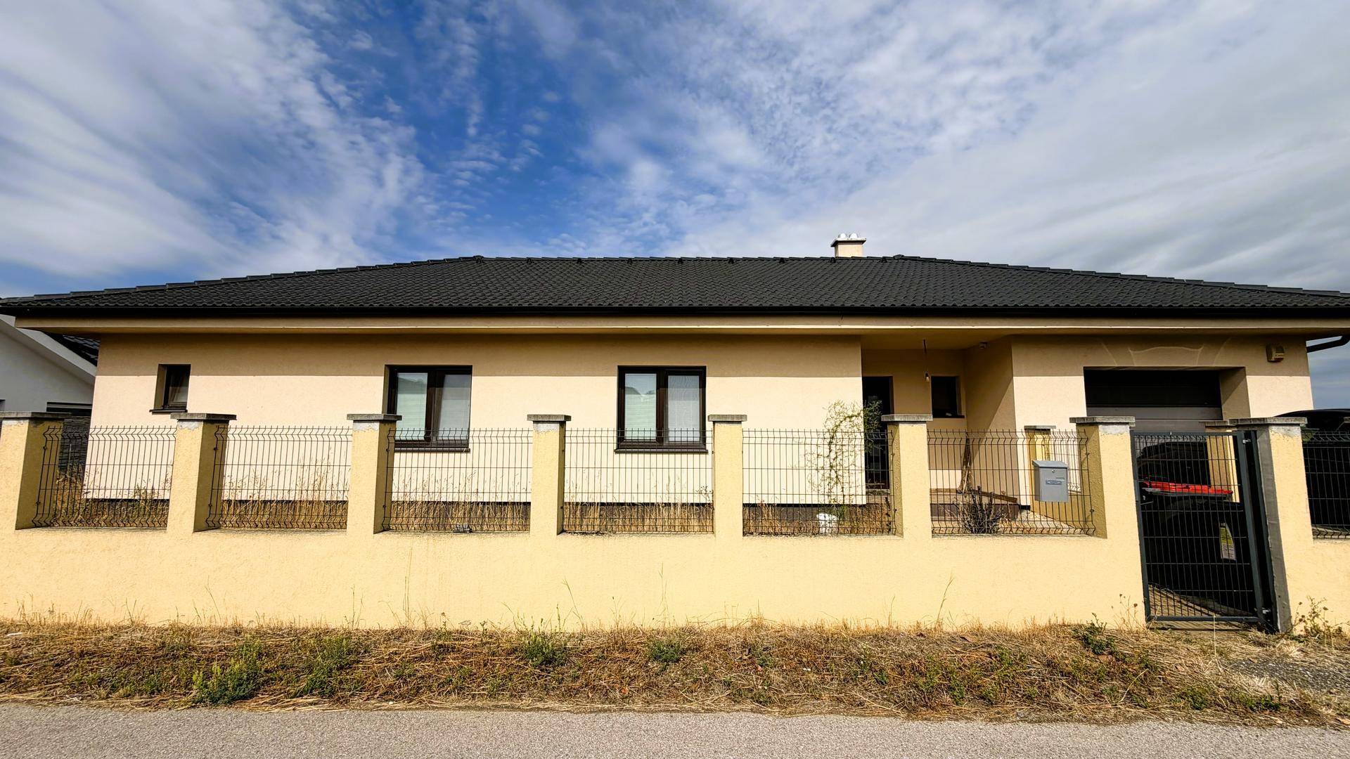 Moderne Hausfassade mit dunklem Dach und Zaun.