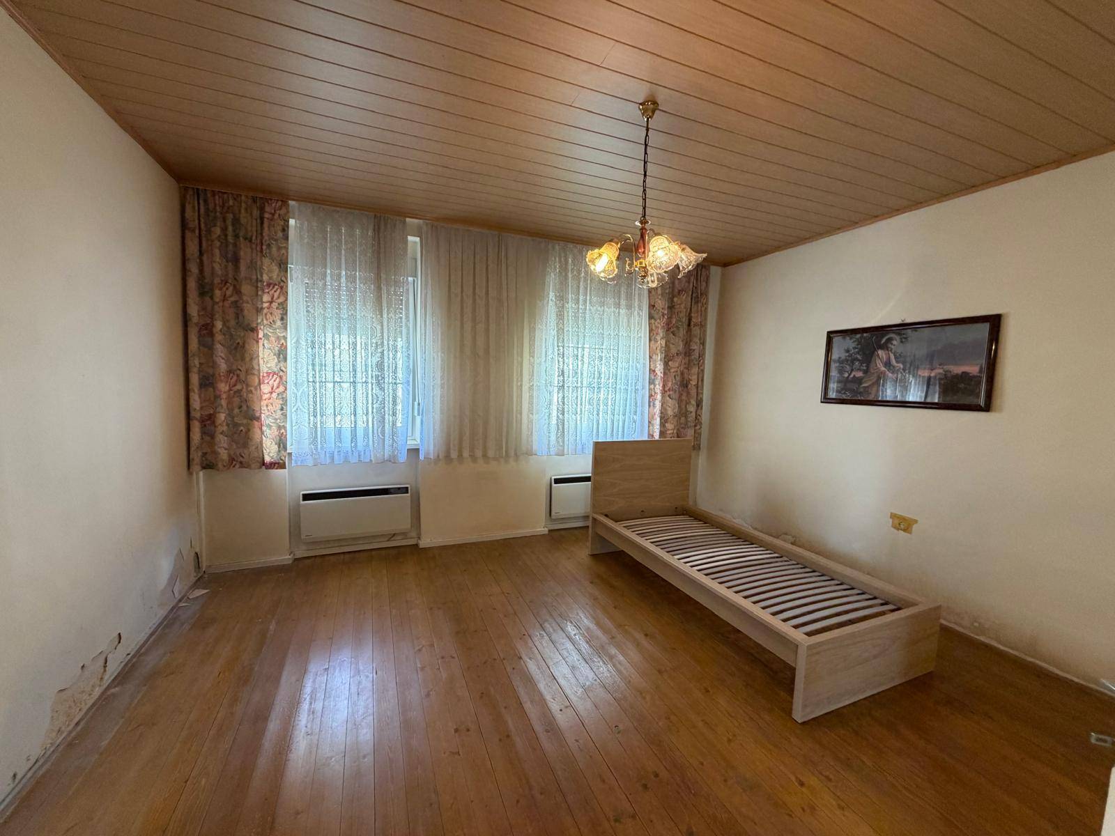 Schlafzimmer mit Holzboden, Holzdecke und einem einfachen Bettgestell.