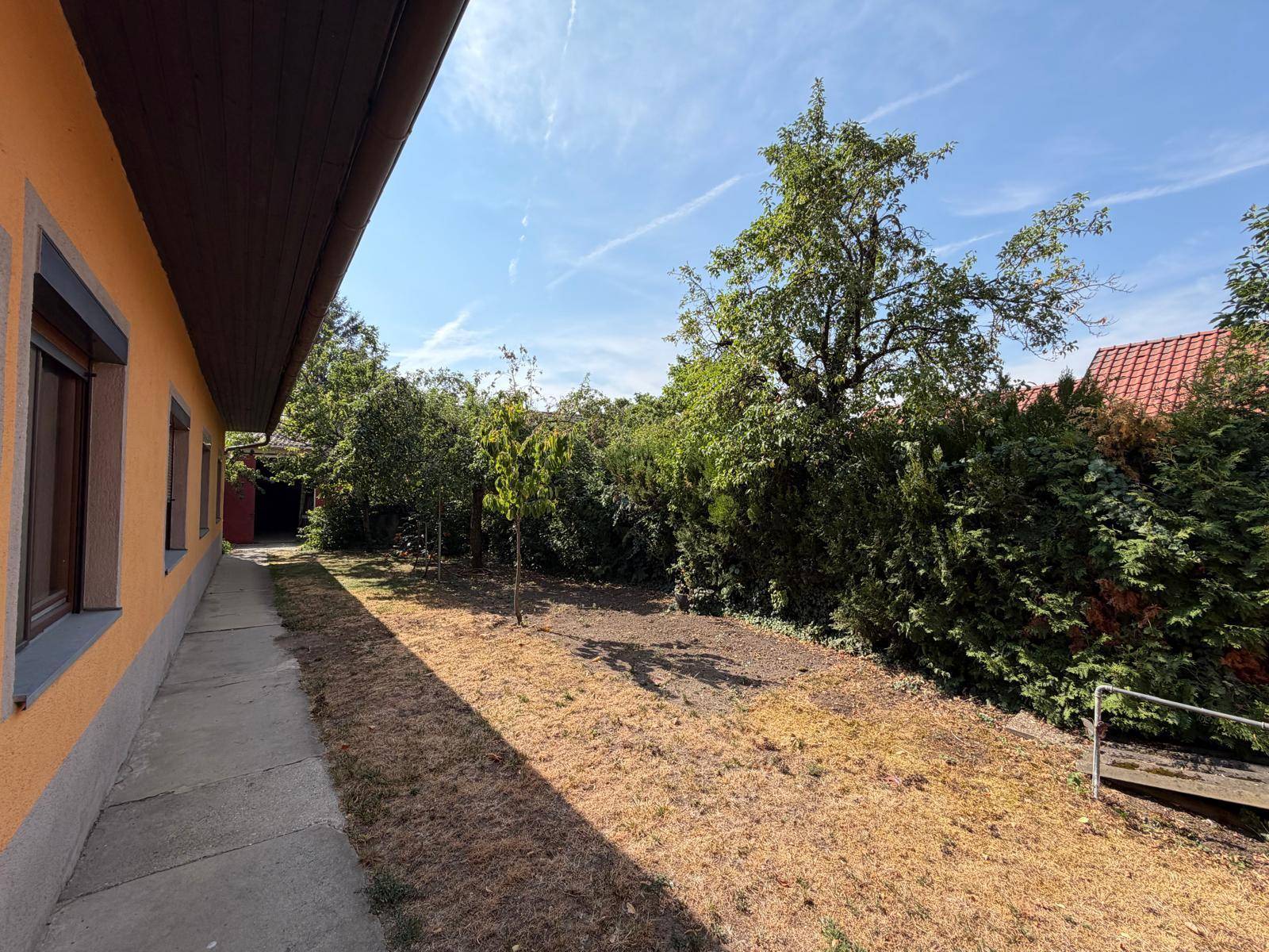 Weitläufiger Gartenbereich neben dem Haus mit trockener Rasenfläche und hohen Hecken.