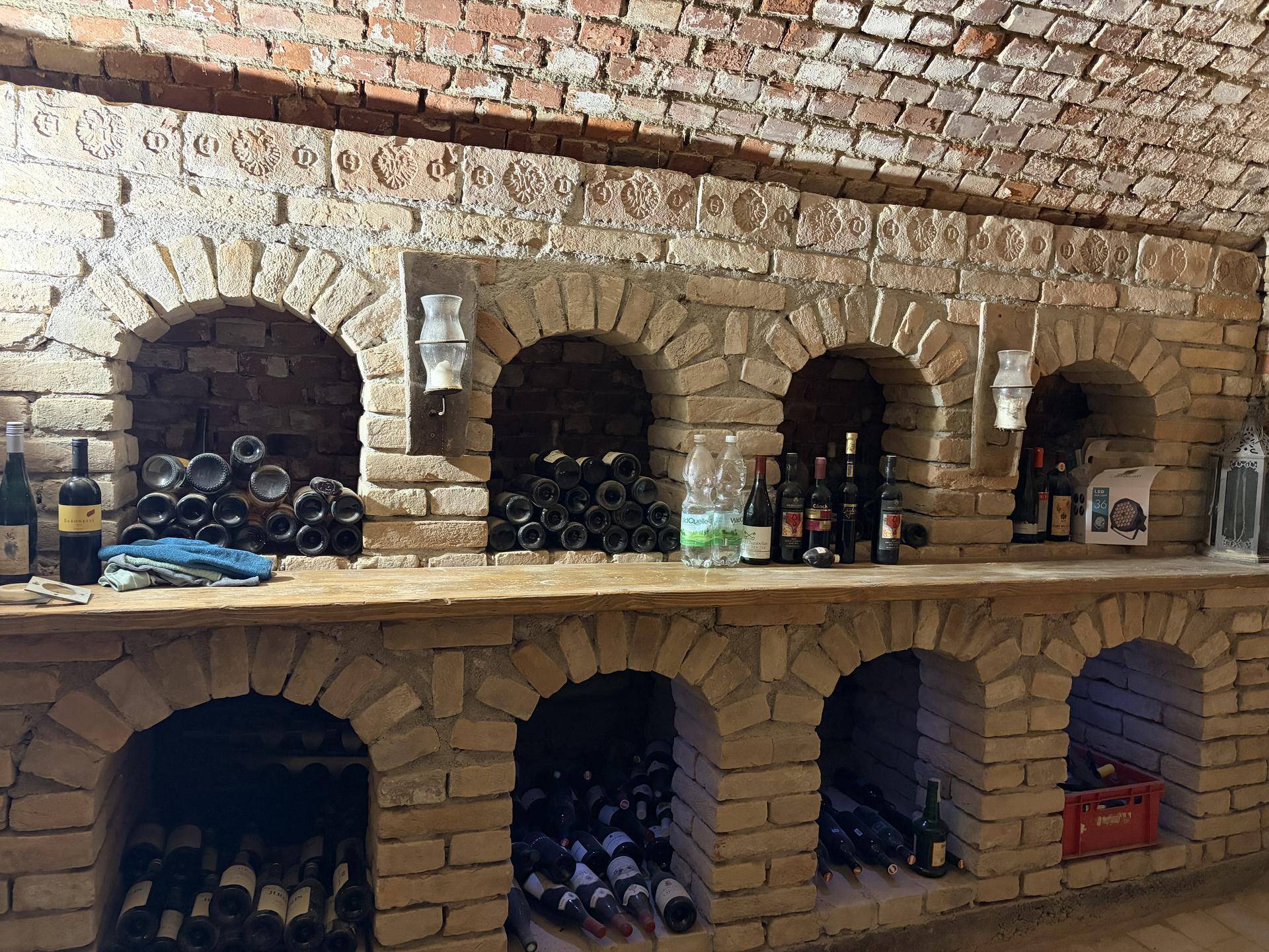 Nahaufnahme der gemauerten Weinregale mit Holzablage und verschiedenen Weinflaschen.