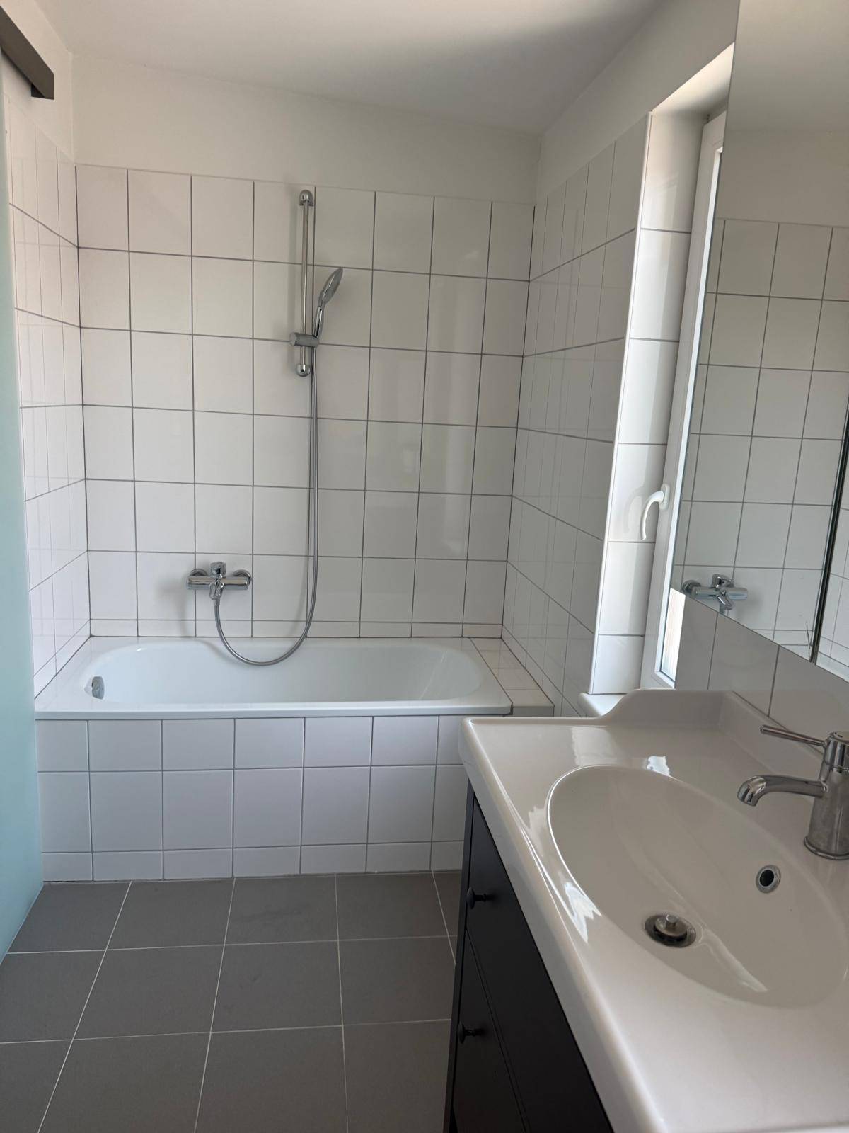 Badezimmer mit Badewanne, Waschbecken und weißen Fliesen.