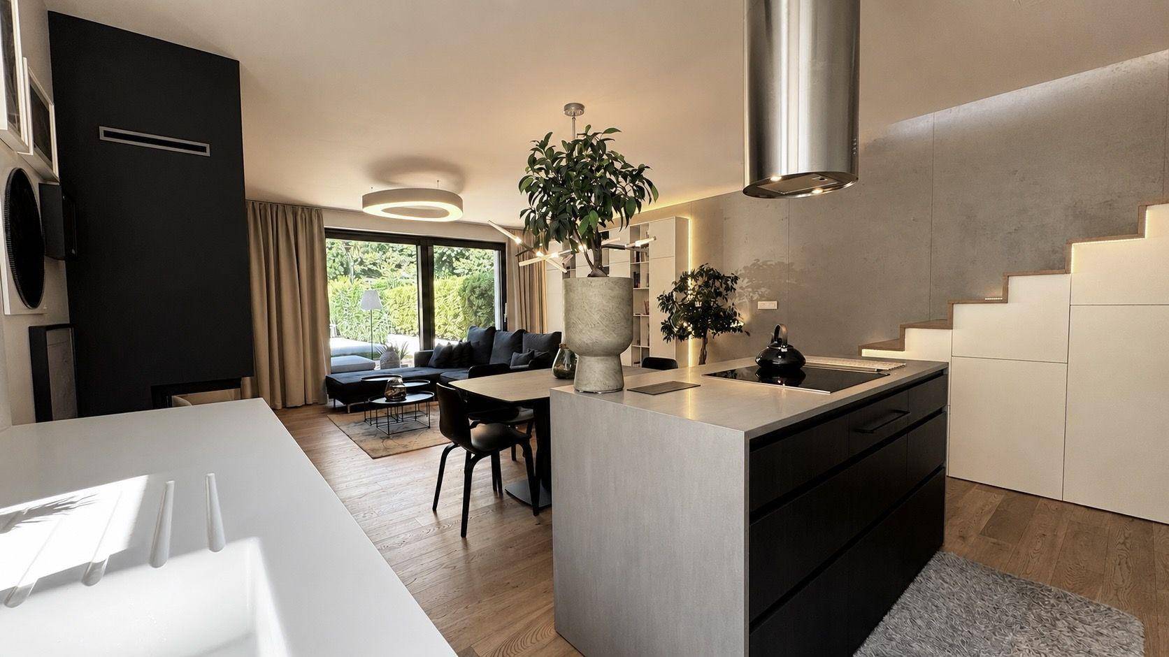 Moderne Küche mit Kochinsel und Blick auf den offenen Wohnbereich mit Kamin und großen Fenstern.