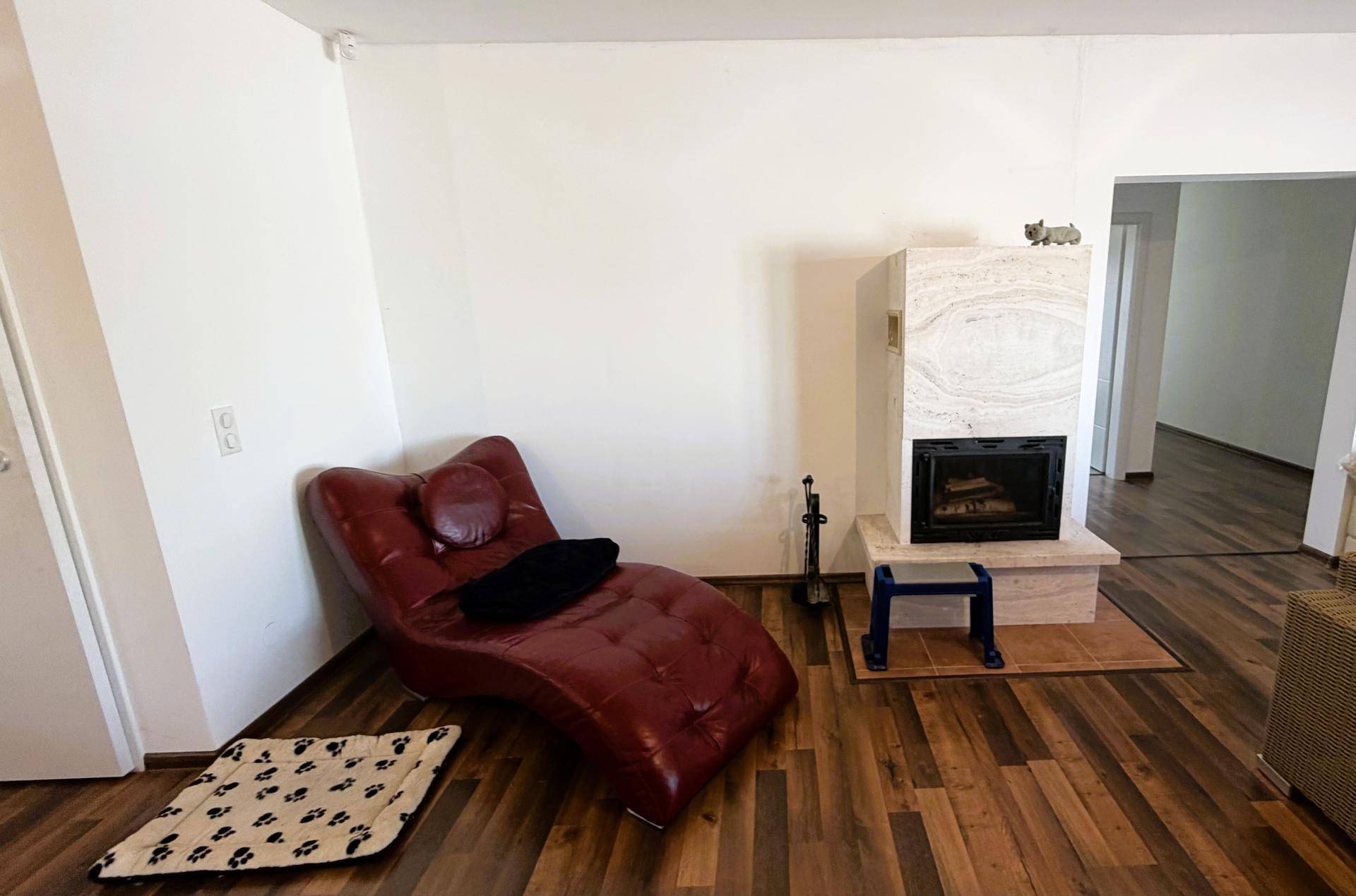 Wohnbereich mit Kamin, roter Chaiselongue und Holzboden.