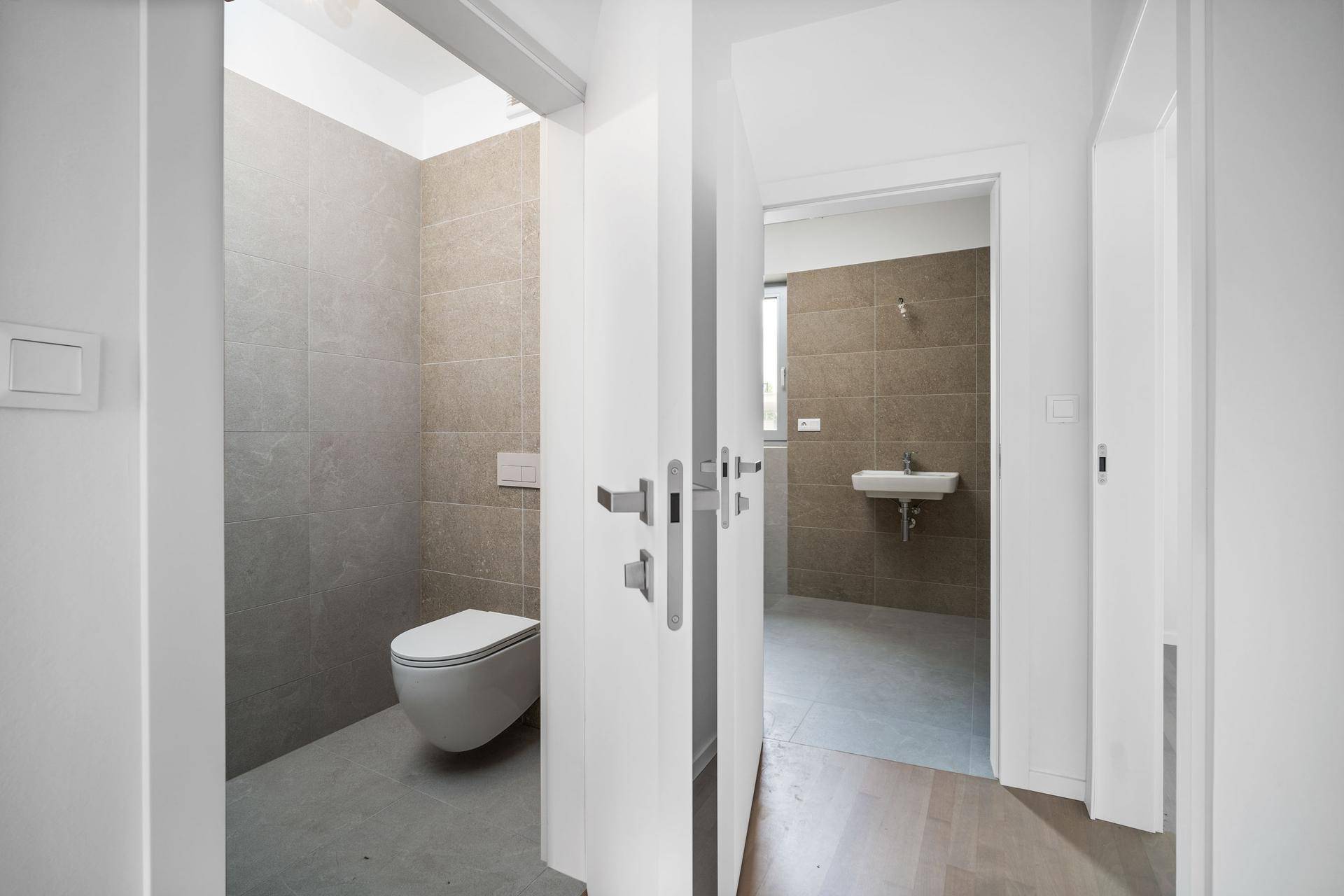 Heller Flur mit Zugang zu einem modernen Badezimmer mit Wand-WC und Waschbecken.