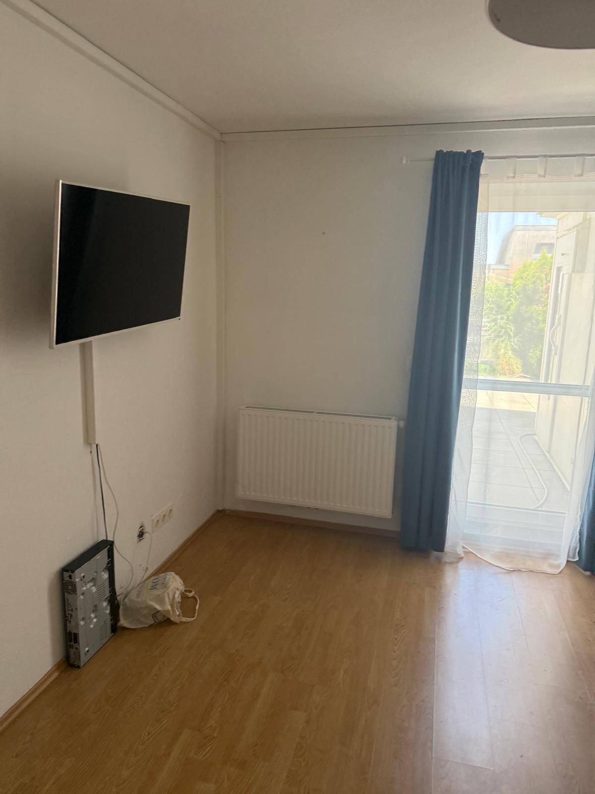 Schlafzimmer mit Wandfernseher, Heizkörper und Zugang zum Balkon.