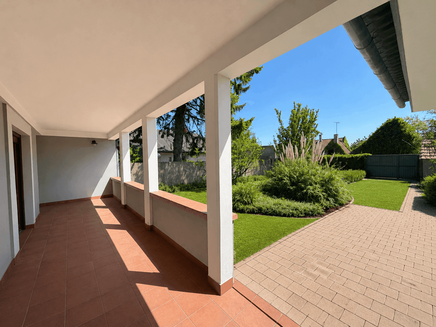 Geräumige überdachte Terrasse mit Fliesenboden und weitem Blick auf den Garten und Rasenfläche.