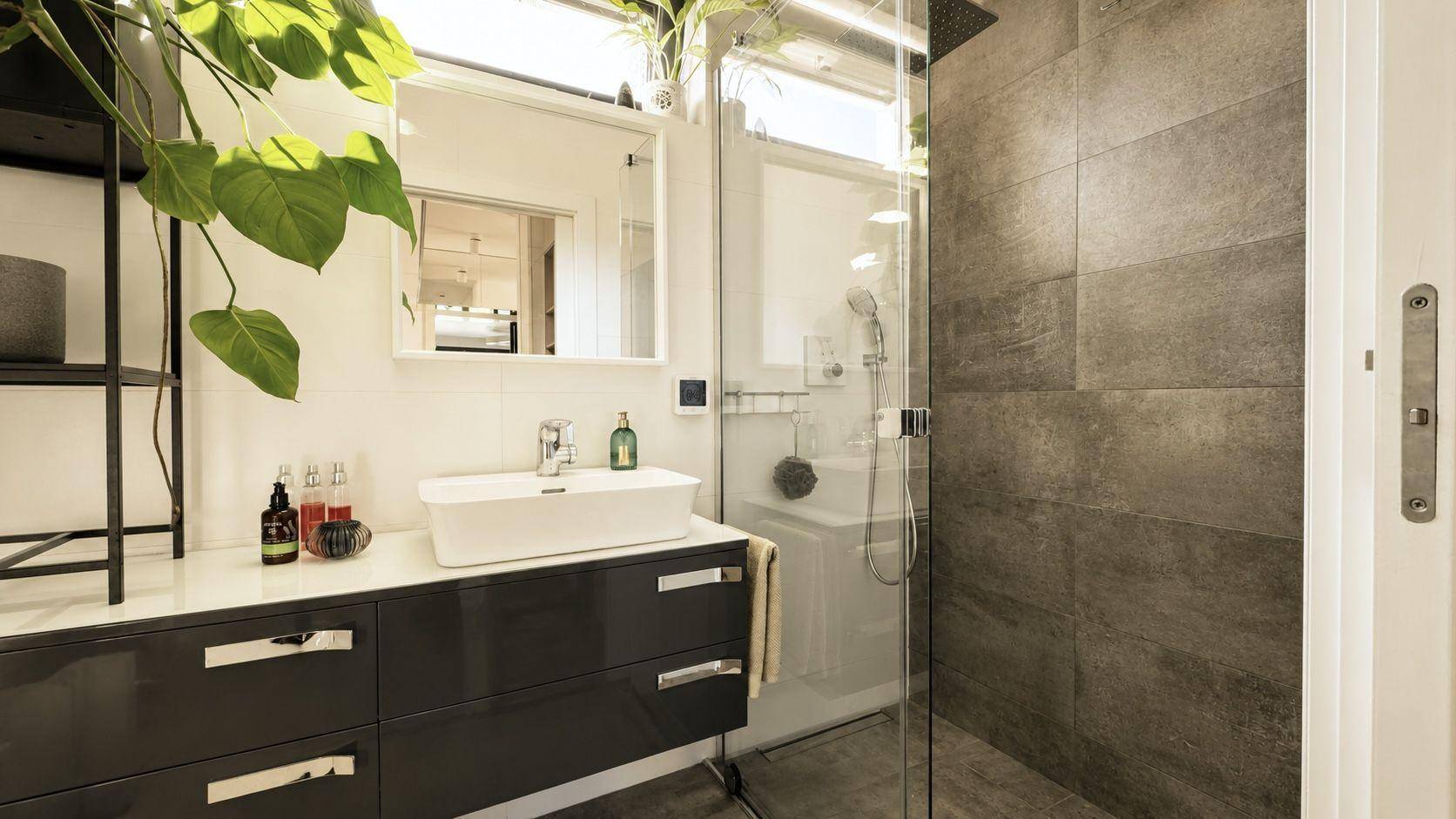 Modernes Badezimmer mit elegantem Waschbecken, dunklem Unterschrank und geräumiger begehbarer Dusche.